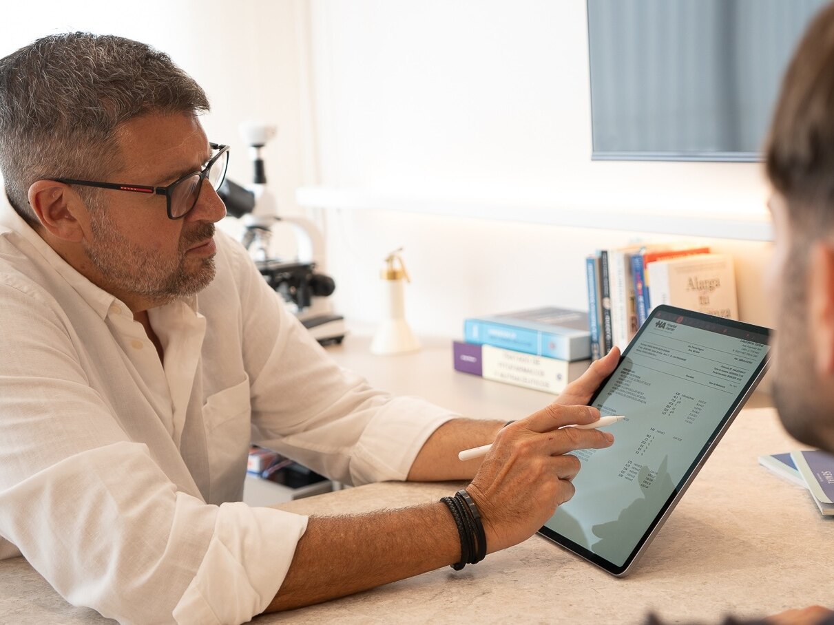 El Dr. Lucchelli repasa resultados en una tablet junto a un paciente, con el microscopio sobre el escritorio