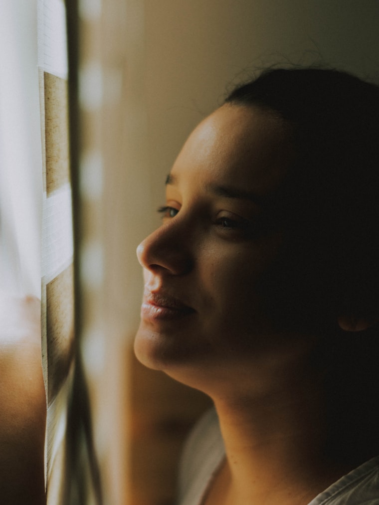 Mujer de perfil junto a una ventana con luz cálida